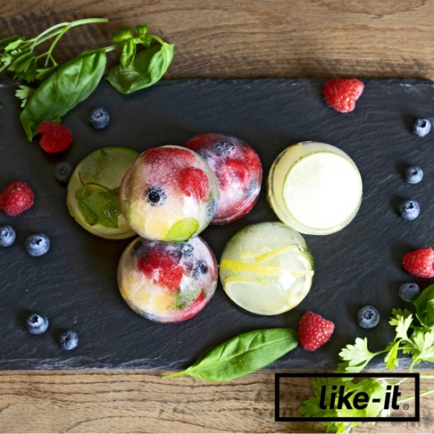 圓形威士忌冰球，內含覆盆子、藍莓、檸檬片與薄荷葉，置於黑色石板上，周圍點綴新鮮水果與香草。