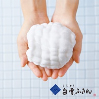 一雙手捧著白色、蓬鬆、多層次的棉質洗澡巾，背景為淺藍色格紋。