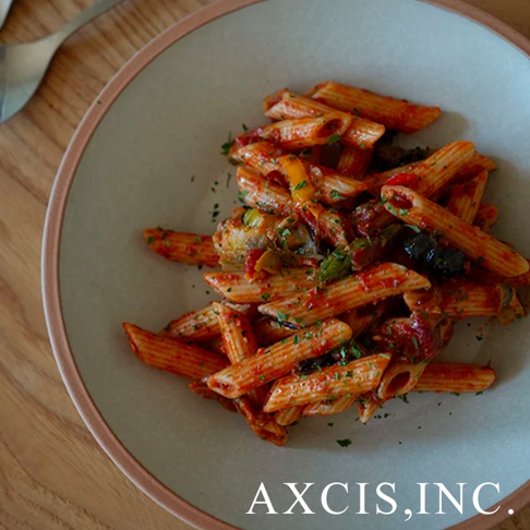 素燒陶瓷義大利麵盤，盤面呈現柔和的淺灰色，邊緣帶有細緻的淡粉色滾邊。盤中盛滿了紅醬筆管麵，麵條裹覆著番茄醬汁，並點綴著切塊的黃椒、橄欖及香草碎。