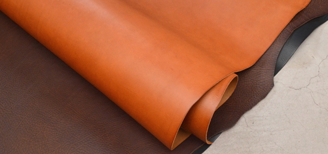 兩塊皮革，一塊為橘棕色，另一塊為深棕色，兩塊皮革堆疊在一起，呈現出材質的紋理與質感。