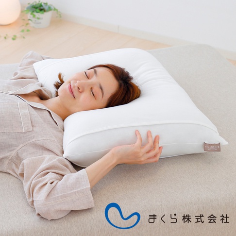一名女子仰臥在床上，頭部枕在一個白色軟枕上。軟枕為純白色，表面平整，帶有細緻的縫線。枕頭的一角有一個淺棕色的標籤，上面印有日文文字。