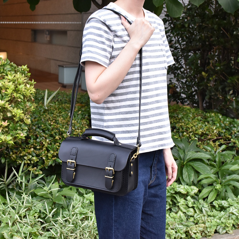 黑色皮革雙扣迷你肩背包，附手提握把，可斜背或肩背，搭配金屬扣環，適合日常穿搭。