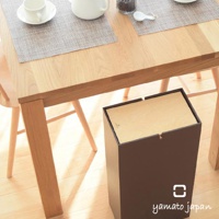 NOPPO 木製風格擺動式垃圾桶，深棕色外觀，頂部蓋子為木紋設計，整體造型簡潔，放置於木質餐桌下方。