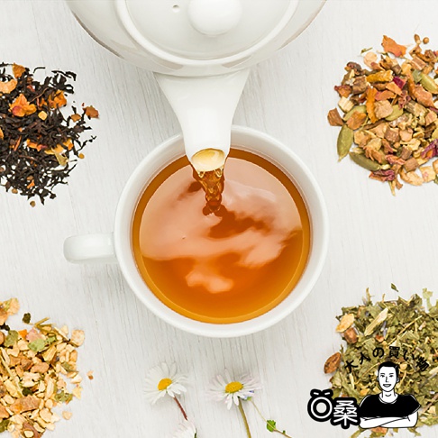 Lakshimi 蜂蜜風味薄荷茶，茶壺正將熱氣騰騰的薄荷茶注入白瓷杯中，周圍散落著乾燥的茶葉、花瓣和香料，以及兩朵小白花，右下角有日文標誌和一個人像剪影