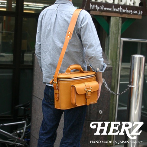 模式B：一位男士身揹日本HERZ手工製作的駝色皮革相機包，包包上有兩個立體口袋，搭配銀色金屬扣環，整體呈現復古風格。