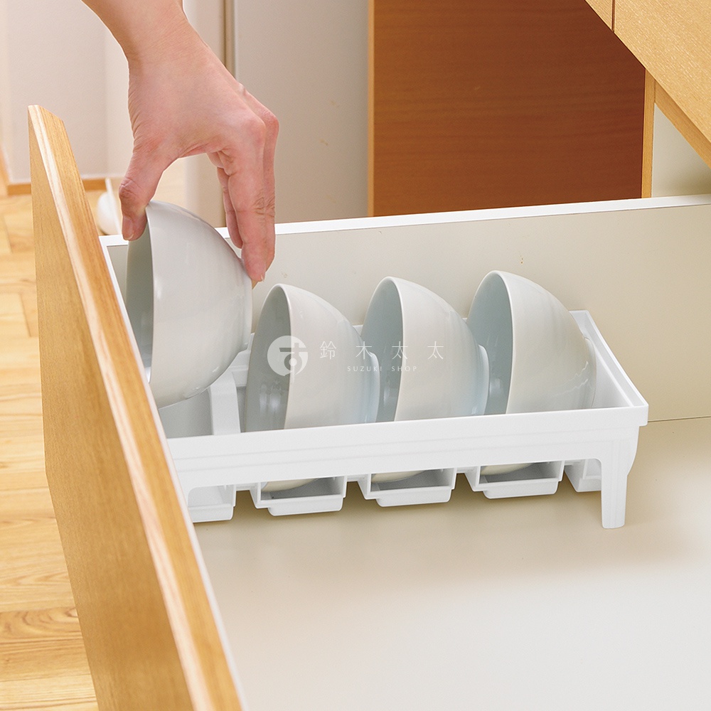 手正在將一個白色碗放入抽屜式餐碗收納架中，收納架內已有三個碗整齊擺放。