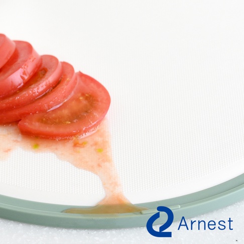 白色抗菌料理砧板，部分區域有切片番茄與番茄汁，砧板邊緣為淺綠色淚滴狀設計。