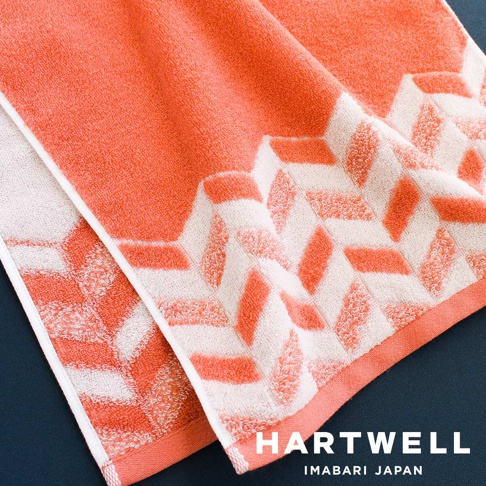 一條珊瑚橘色與白色交織的今治浴巾，以傳統幾何圖紋織成，觸感細緻，適合日常使用。