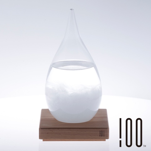 透明玻璃製成的水滴狀天氣瓶，內部裝有液體及白色羽毛狀物質，瓶身置於方形木製底座上，整體呈簡約風格。