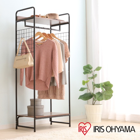 黑色金屬框架吊掛衣架，頂部有木紋層板，下方有網狀掛衣區，吊掛多件粉色、米色、灰色衣物，左側懸掛一個米色側背包，下方有兩層木紋置物板，底部置物板上擺放兩個灰色圓形收納盒。