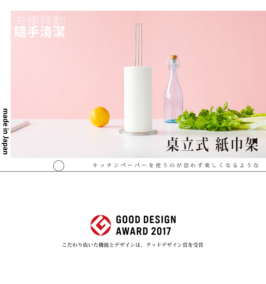 不鏽鋼立式紙巾架，帶有圓形底座，架上裝有白色紙巾捲，旁邊有橙色水果、透明玻璃瓶和綠葉蔬菜。