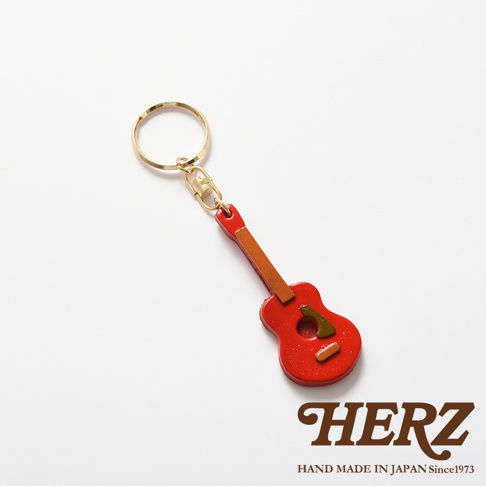 職人手作皮革吉他造型鑰匙圈，主體為紅色皮革，點綴有棕色皮革細節，搭配金色鑰匙圈。