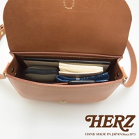 職人手作皮革經典馬鞍包 CK-7 S，採用淺棕色皮革製成，包內可見筆記本、零錢包、手機及藍色印花布料，設計簡潔實用。