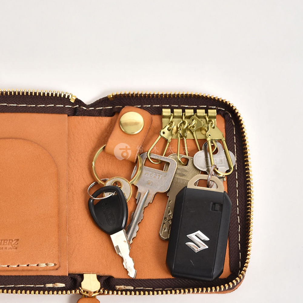 職人手作皮革多用途收納鑰匙包，展示棕褐色皮革內襯，裝有數串鑰匙、汽車遙控器及黃銅色鑰匙扣，側邊有拉鍊及品牌標誌。