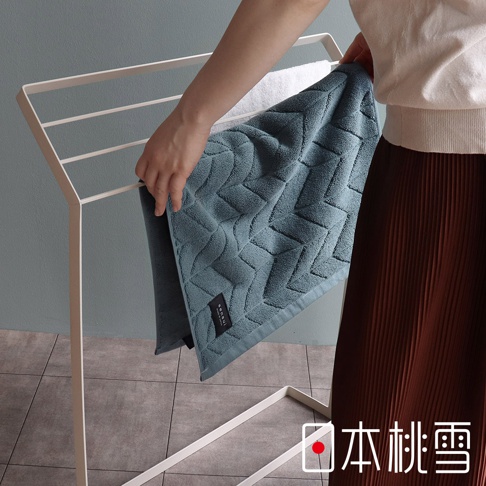 一條藍綠色、帶有菱形紋路的高密度吸水浴墊，標籤上有「sensui」字樣，被一隻手放在白色晾衣架上。