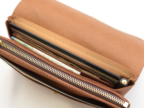 職人手作皮革旅行長夾，淺棕色牛皮材質，內有護照、機票、紙鈔和一支筆，拉鍊為金色。