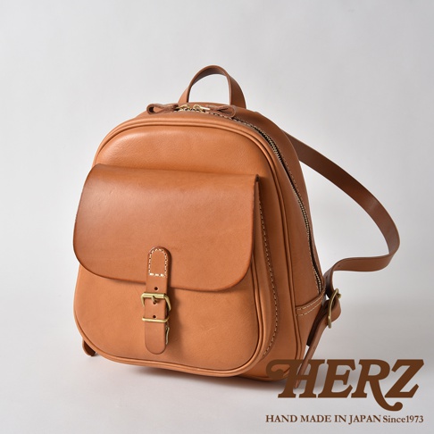 職人手作皮革立體口袋迷你後背包，採用天然皮革材質，呈現溫潤的棕褐色澤。包款設計簡潔，設有立體前袋，以皮帶和金屬釦環固定，頂部為拉鍊開口，配有雙肩帶。