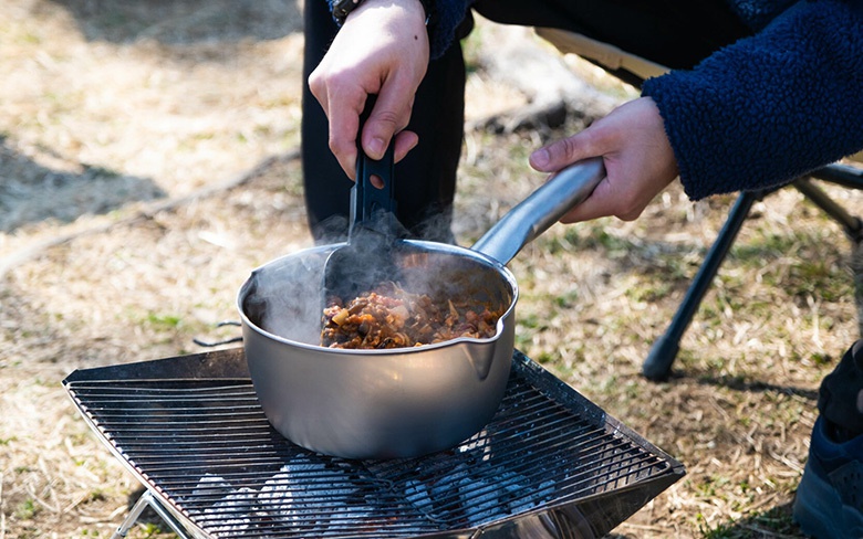 一個圓形、銀色不鏽鋼雪平鍋，裝有烹煮中的食物，鍋身散發蒸氣，鍋柄為銀色，鍋子放在燒烤架上。