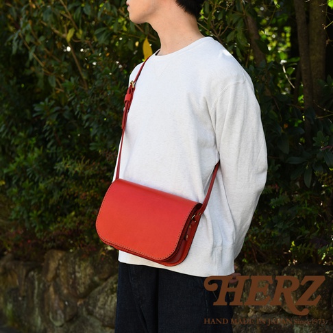 職人手作紅色皮革翻蓋橫式單肩包，採用光滑皮革材質，設計簡約，搭配可調式肩帶，展現經典風格。