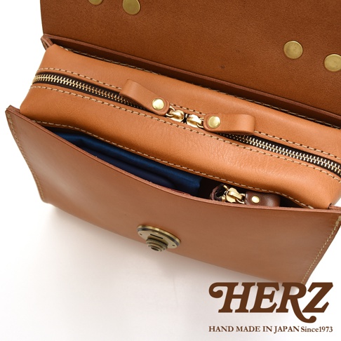 HERZ 職人手作皮革多功能收納單肩包，特寫內部拉鍊和收納空間，下方為品牌 LOGO 和「HAND MADE IN JAPAN Since1973」字樣。