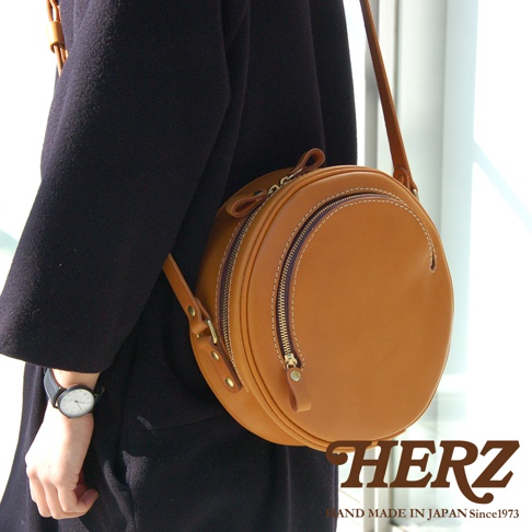 職人手作皮革小圓包 CK-19 M，採用光滑棕色皮革製成，圓潤造型，配有雙拉鍊開口及皮革拉環，可肩背或斜挎。