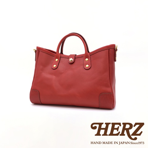 紅色皮革大容量托特包，有兩個手提把，正面中央有一個旋轉鎖扣，兩側裝飾有金屬卯釘，包包底部四角有加固皮革。