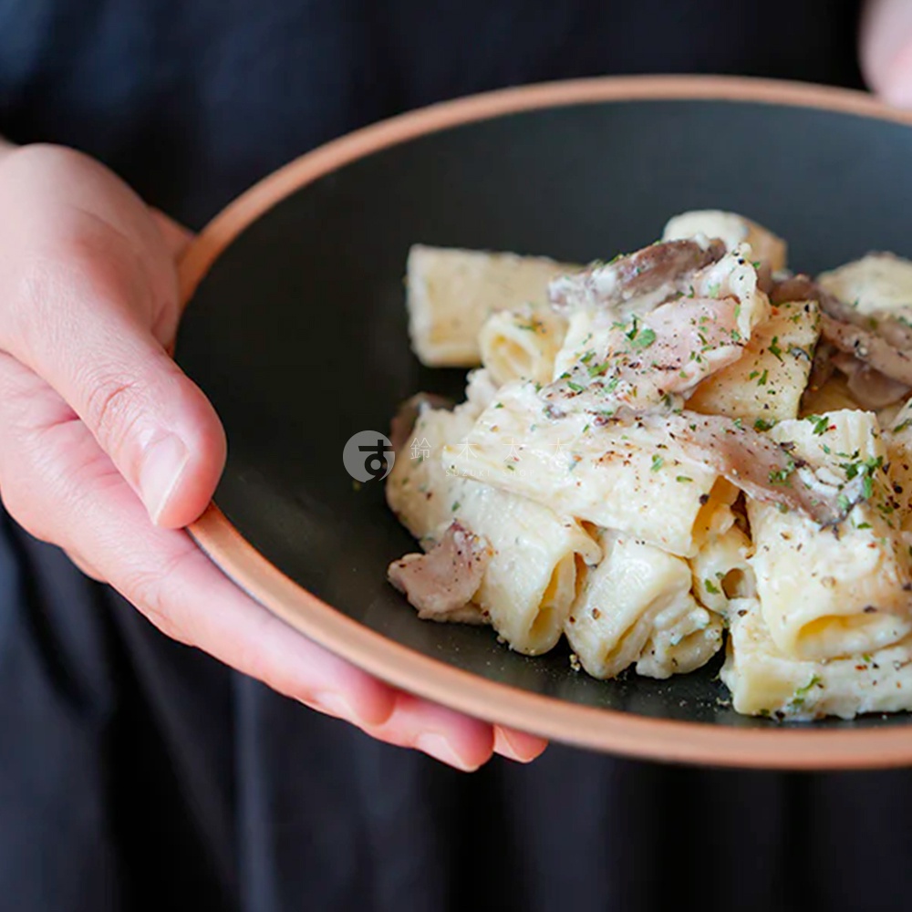 素燒陶瓷義大利麵盤，盛裝著奶油蘑菇義大利麵，盤邊帶有淺棕色外緣。