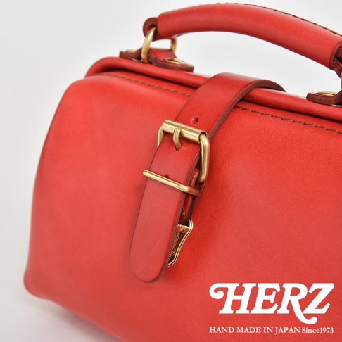 紅色皮革迷你軟皮手提包，配有黃銅釦環和皮革提把，包身縫線清晰可見。
