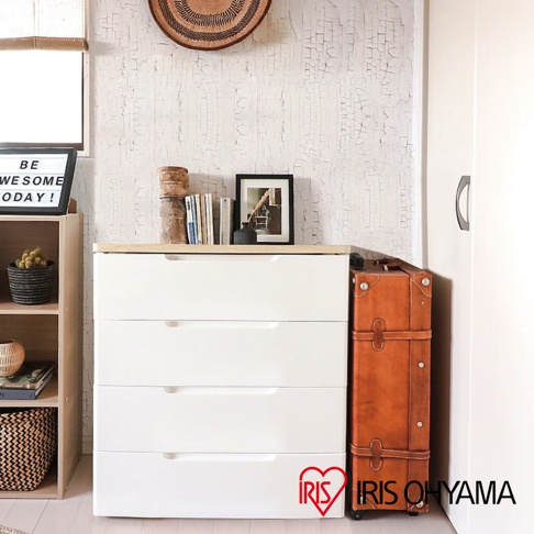 四層白色木質收納櫃，配有木紋頂板，抽屜面板上有隱藏式把手，旁邊有一個棕色復古皮箱。