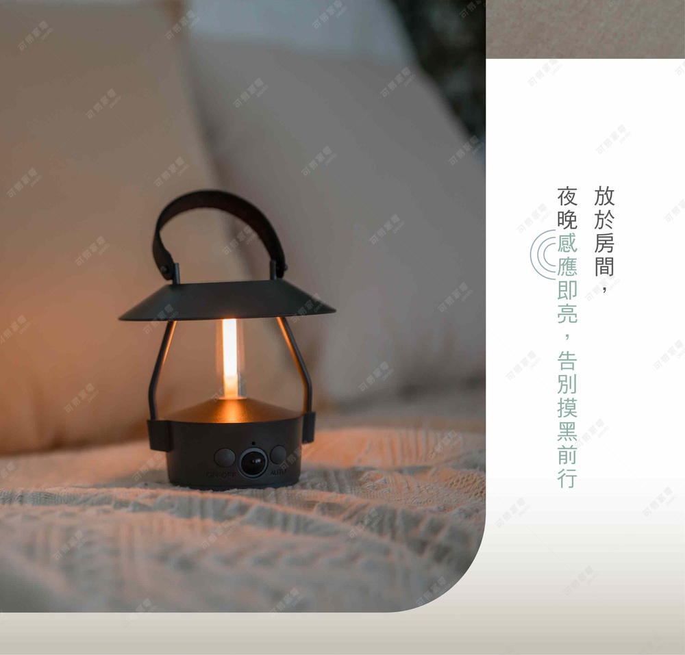 一個黑色金屬材質的復古風格LED感應燈，帶有提把，燈泡發出暖黃色光，底部有兩個按鈕，整體放置在柔軟的白色織物上。