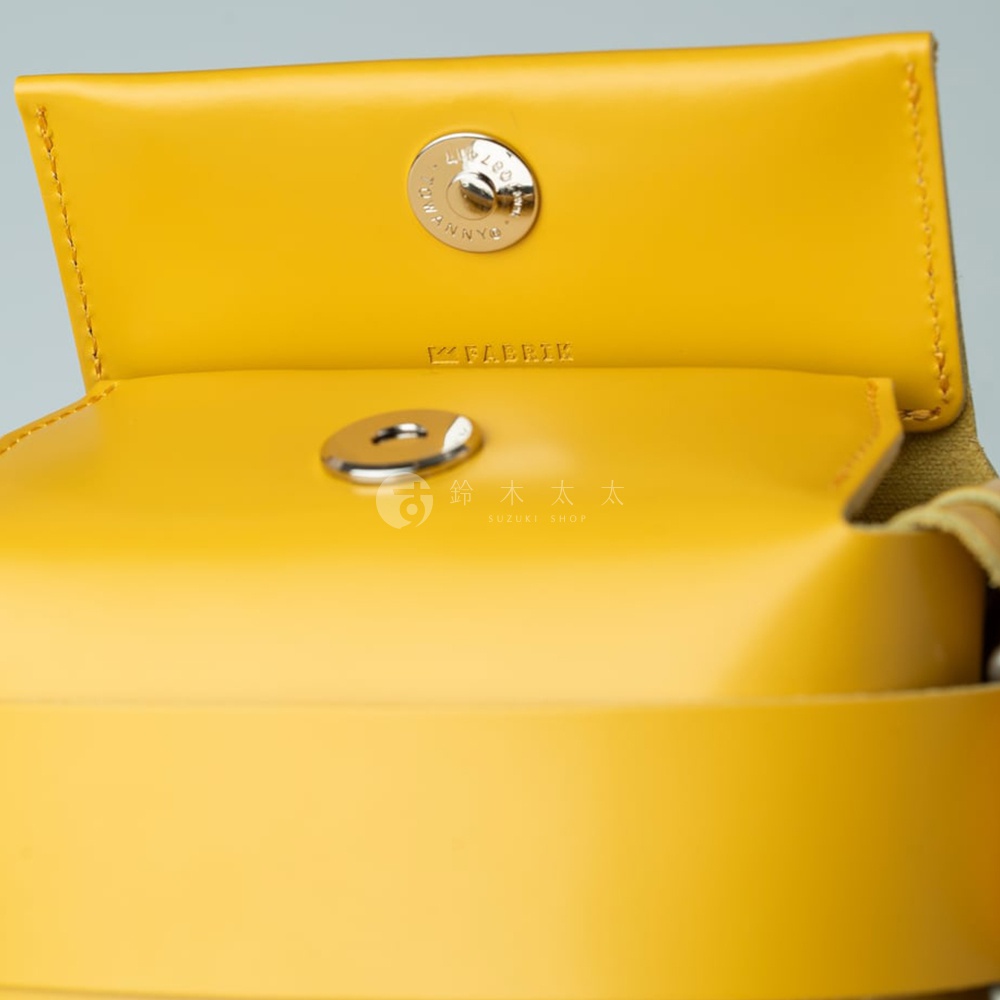 以黃色皮革製成的迷你斜背包，展示內部金屬按鈕和 FABRIK 品牌標誌。