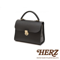 HERZ 職人手作黑色皮革手提包，配有金色鎖扣和拉鍊細節，下方印有品牌標誌。