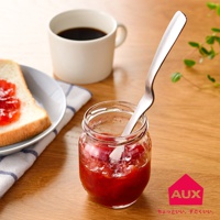 銀色金屬製的不沾桌果醬抹刀，插入裝有紅色果醬的透明玻璃罐中，一旁有塗抹果醬的吐司和一杯咖啡。