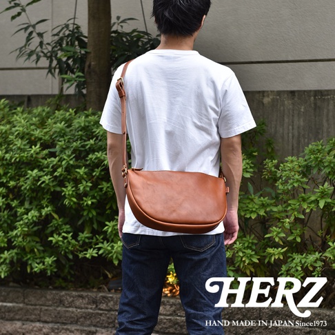 日本HERZ職人手作皮革半圓馬鞍包，棕色皮革，從背面拍攝，包包斜挎在身，搭配牛仔褲。