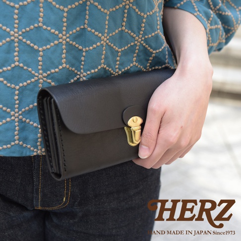 職人手作黑色皮革長夾，具手風琴式多卡層設計，搭配金色金屬釦，由手持展示。