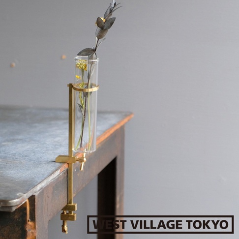 黃銅可夾式玻璃花器，帶有兩支裝飾性植物，一個透明圓筒形玻璃試管，固定在黃銅夾具上，夾具夾在桌子邊緣。