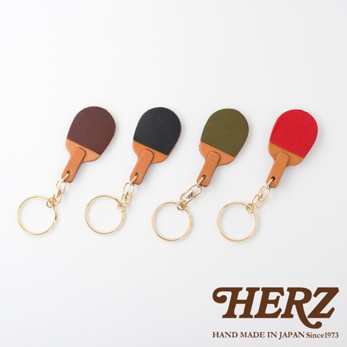 四個職人手作皮革桌球拍造型鑰匙圈，分別為深棕色、黑色、軍綠色和紅色，搭配皮革柄與金色金屬扣環。