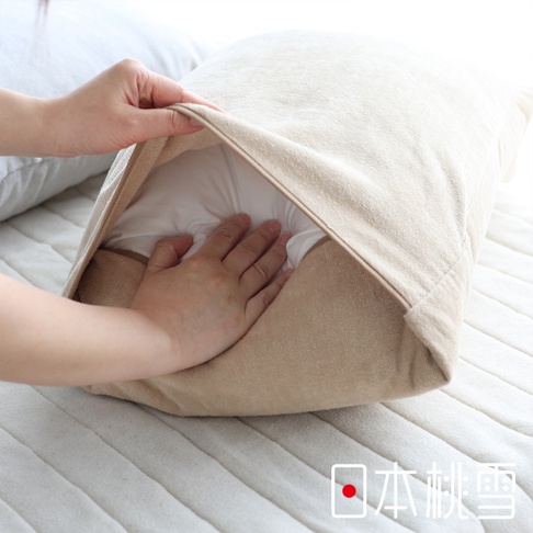 一隻手正將一個米白色絲絨風毛巾材質的枕套套入白色枕芯中，展現其柔軟透氣的質感。