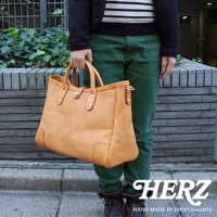 一款淺棕色皮革托特包，包身結構分明，配有兩條皮革提把，包口中央有一個金屬旋扣。