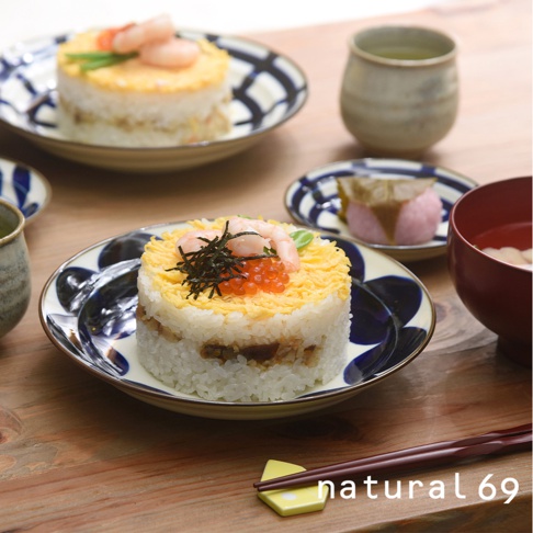 焦吳須圓盤，以白色壽司飯為底，中間層夾雜著醬汁雞肉或鳗魚，頂部鋪滿金黃炒蛋絲，並綴以鮮紅鮭魚卵、綠色蔥絲及兩隻粉色熟蝦，整體呈圓柱狀，擺放在藍白花紋陶瓷盤上。