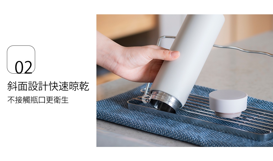 手持白色金屬保溫杯，放置在銀色不鏽鋼折疊瀝水架上，底部有藍色紋理布墊。