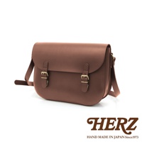 棕色皮革製成的經典馬鞍包，配有兩個黃銅色搭扣和可調節的肩帶，包身線條圓潤，設計簡潔。