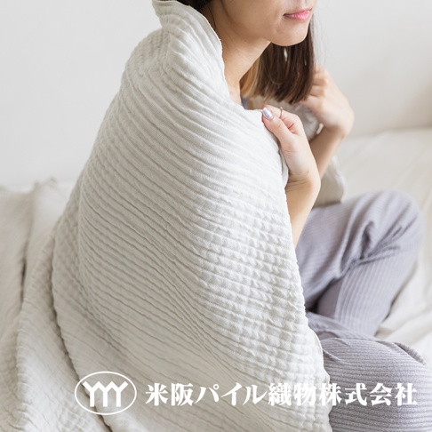 一位女士被一條米白色三層紗輕透波紋毯包裹，毯子呈現細緻的波紋紋理。