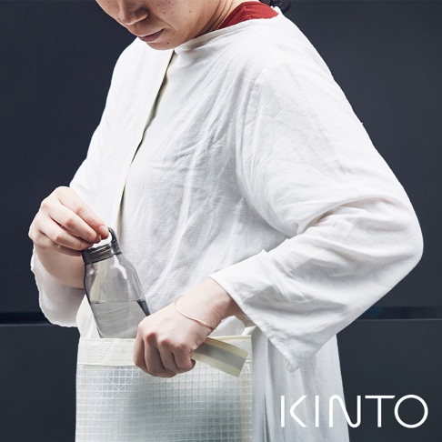 一名女子將透明玻璃輕水瓶放入白色網格紋理的布袋中。水瓶為灰色瓶蓋，容量約為500毫升。