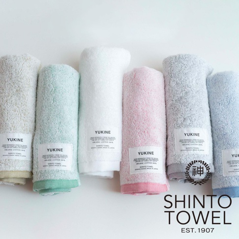 YUKINE 雪中漫步系列有機棉蓬厚浴巾，展示了米白、淺綠、純白、粉紅、淺灰及淺藍六種顏色，浴巾質地蓬鬆柔軟，標籤顯示為有機棉材質，產地為日本大阪。
