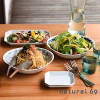 白色橢圓形麵食盤，飾有藍色花紋，內含義大利麵食，盤旁為藍色玻璃杯、金屬餐具及一小碟白色點心盤，另有兩份沙拉盛裝於白色盤中，背景為木質桌面。