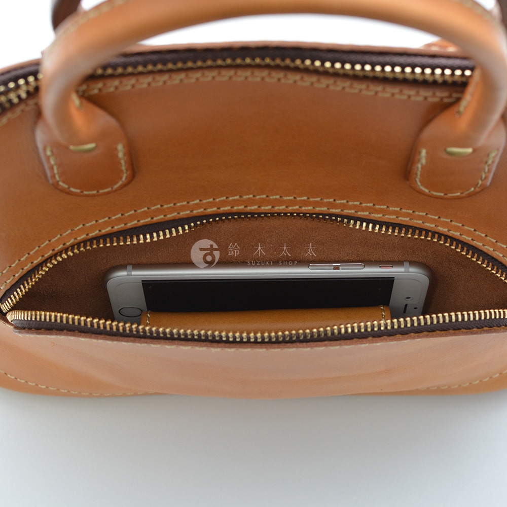 職人手作皮革兩用經典貝殼手提包，採用棕色皮革，包身拉鍊開口內可見一支銀色手機，整體呈現經典復古風格。