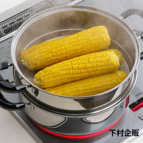 不鏽鋼雙層蒸氣料理鍋，鍋內有三根金黃色玉米正在蒸煮，鍋身帶有兩個黑色隔熱手柄，置於電磁爐上，鍋底有紅色加熱指示。