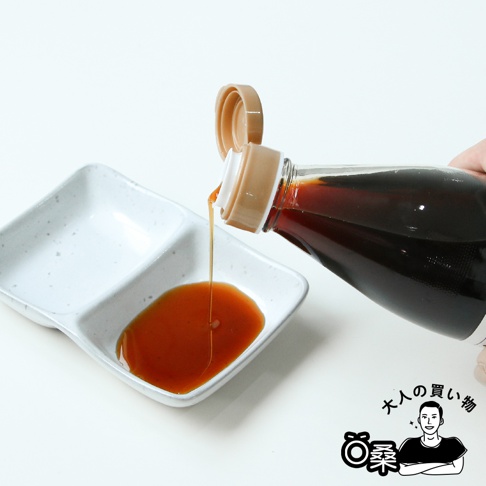深褐色壽喜燒沾醬從透明塑膠瓶中傾倒至白色雙格陶瓷醬料碟中，醬料呈琥珀色，瓶蓋為米白色，有日文品牌標誌。