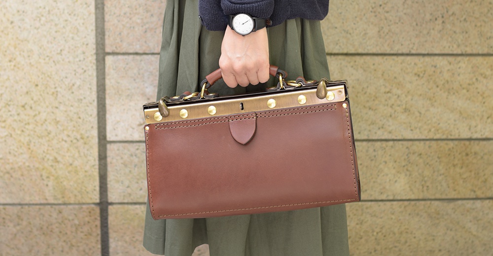 棕色皮革復古口金兩用手提包，配有金色金屬配件和皮革提把，適合手提或肩背。